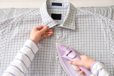 Ekose gömleği ütüleyen kadın evde, yakın plan.