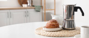 Geyser coffee maker with delicious bun and cup of espresso on table in kitchen