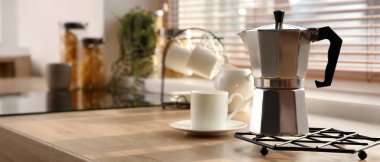 Mutfak tezgahında gayzer kahve makinesi ve fincanı var.