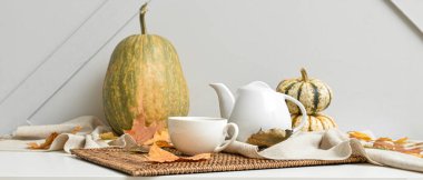 Çay demliği, bir fincan sıcak içecek, balkabağı ve sonbahar yaprakları gri duvarın yanındaki masada.