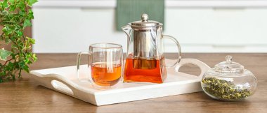 Çaydanlıklı tepsi ve mutfaktaki masada bir bardak sıcak içecek.