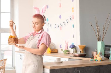 Tavşan kulaklı genç bir kadın ve mutfakta paskalya yumurtası sepeti.