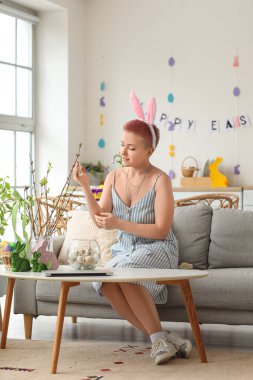 Evde Paskalya yumurtasıyla ağaç dallarını süsleyen genç bir kadın.