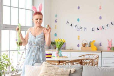 Evde tavşan kulaklı ve paskalya yumurtası olan genç bir kadın.