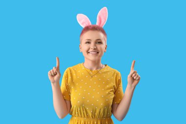 Tavşan kulaklı genç kadın mavi arka plandaki bir şeyi işaret ediyor. Paskalya kutlaması