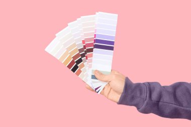 Pembe arka planda boya paletleri olan bir erkek el.