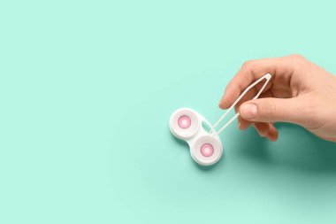 Cımbızlı kadın elleri ve turkuaz arka planda kontak lensli konteynır