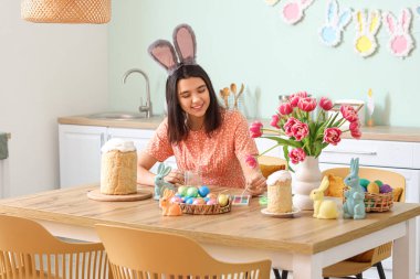 Tavşan kulaklı güzel bir kadın mutfakta paskalya yumurtası boyuyor.
