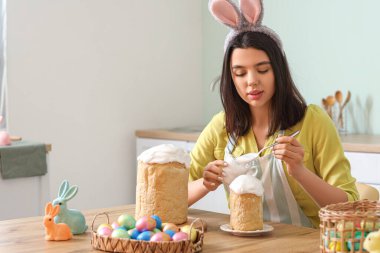 Tavşan kulaklı güzel bir kadın mutfakta paskalya pastası süslüyor.