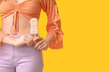 Sarı arka planda beyaz çikolata kaplı çilekli dondurma tutan genç bir kadın.