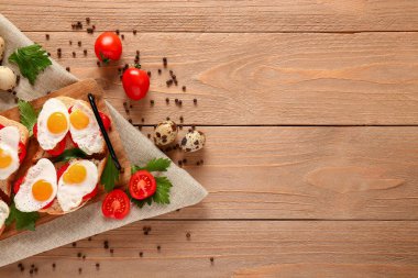 Kızarmış bıldırcın yumurtalı, domatesli ve ahşap arka planda baharatlı lezzetli sandviçler.