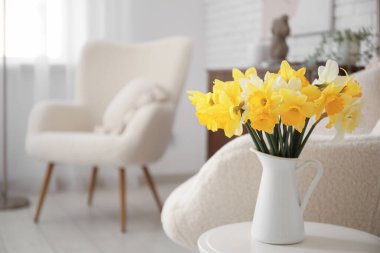 Oturma odasının içinde nergis çiçekleri olan rahat koltuklar ve kahve masası.