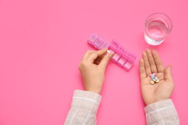 Haplı kadın elleri ve pembe arka planda bir bardak su.