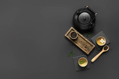 Fincanlı çaydanlık, bir kaşık kuru çay ve siyah arka planda yapraklar.