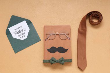 Bej arkaplanda Mutlu Babalar Günü 'nü anlatan bir zarf içinde süslü kitap ve kağıt. Üst görünüm