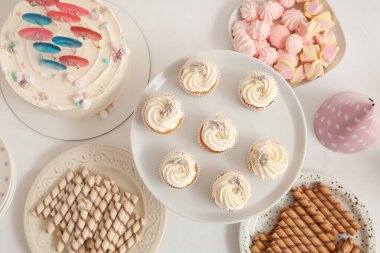 Beyaz masadaki doğum günü partisi için tatlı standında lezzetli kekler ve diğer tatlılar.