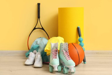 Spor malzemeleri, çanta, paten ve spor ayakkabıları sarı duvarın yanında.