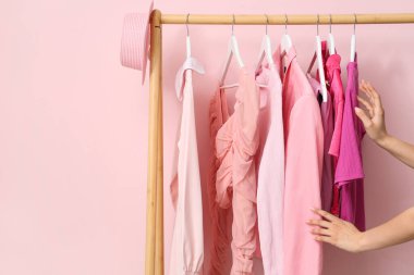 Kadın elleri, pembe duvarın yanında elbiseleri olan askılara dokunuyor.
