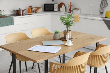 Kahve fincanlı dizüstü bilgisayar ve mutfaktaki yemek masasında bitkiler.