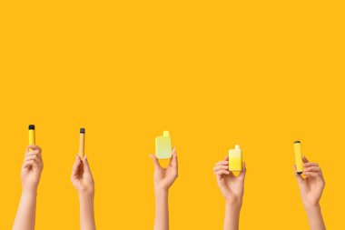 Sarı arka planda elektronik sigaraları tutan bir sürü el var.