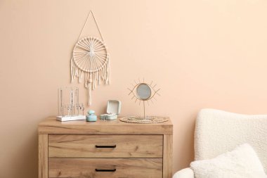 Bej duvarın yanındaki dolapta farklı mücevherler, ayna ve parfüm şişesi olan organizatörler.