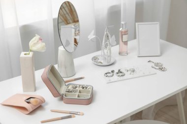 Pencerenin yanındaki masada farklı takılar, ayna ve fotoğraf çerçevesine sahip organizatörler