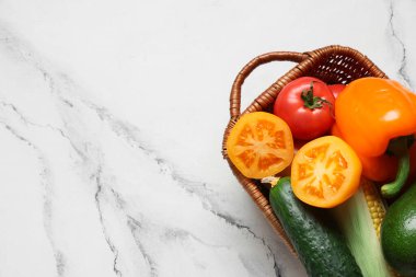 Beyaz arka planda farklı taze sebzeler bulunan hasır sepet, yakın plan.