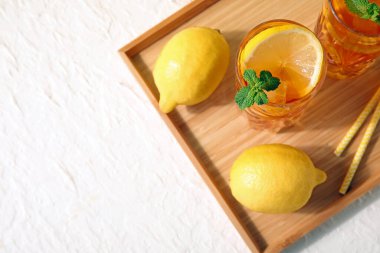 Tahta tepsi, lezzetli soğuk buzlu çay bardakları ve beyaz grunge arka planda limonlar.