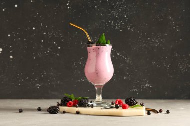 Bir bardak taze meyve püresi, farklı meyveler ve gri masada nane şekeri.