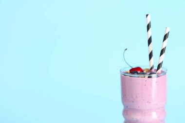 Mavi arka planda yabanmersinli, kirazlı ve fındıklı bir bardak taze meyve püresi.