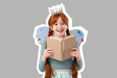 Peri kostümlü küçük kızıl kız, gri arka planda kitap okuyor.