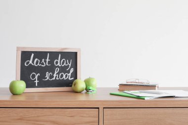 Okulun son günü yazılı tebeşir tahtası, ışık duvarının yanındaki masada elmalar ve defterler
