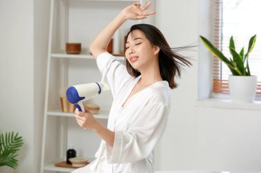 Güzel Asyalı bir kadın banyoda saçlarını kurutuyor.