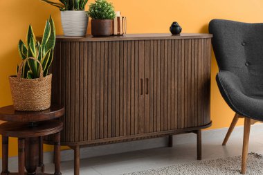 Kahverengi ahşap çekmeceler. Çiçekler ve turuncu duvarın yanındaki sandalye.