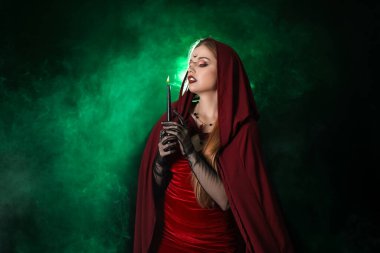 Koyu yeşil arka planda mumu olan güzel genç cadı.