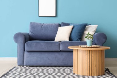 Mavi duvarın yanında yastıklı ve ahşap sehpalı rahat bir kanepe.