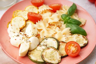 Beyaz arka planda domatesli ve fesleğenli lezzetli makarna salatası.