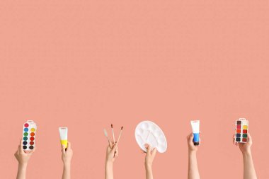 Pembe arka planda sanatçı malzemeleri olan kadın eller.