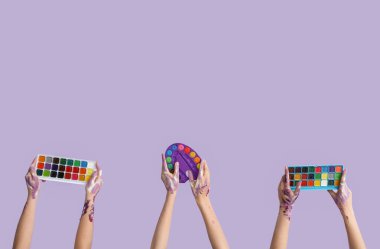 Paletli kadın elleri ve leylak arkaplanlı suluboya boyalar.