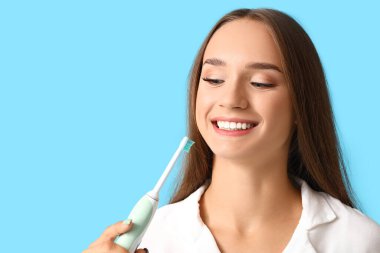 Mavi arka planda diş fırçası olan gülümseyen genç kadın, yakın plan.