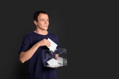 Karanlık arka planda oy sandığı olan genç adam