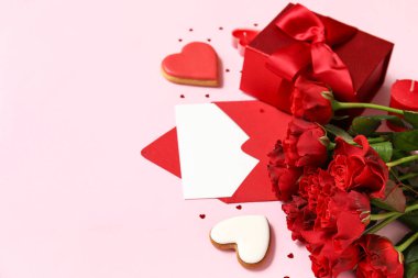 İçinde boş tebrik kartı, kalpler, hediye kutusu ve pembe arka planda bir buket gül olan bir zarf. Sevgililer Günü kutlaması