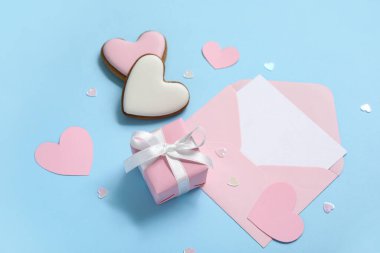 Kalp şeklinde kurabiyeler, zarf ve mavi arka planda hediye kutusu. Sevgililer Günü kutlaması