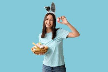 Tavşan kulaklı ve mavi arka planda Paskalya sepeti olan güzel bir genç kadın.