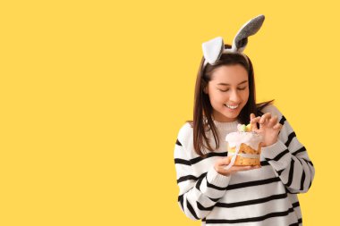 Tavşan kulaklı güzel bir genç kadın ve sarı arka planda Paskalya pastası.