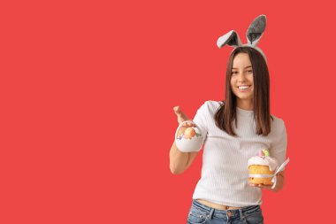 Tavşan kulaklı güzel bir kadın, kırmızı arka planda Paskalya pastası ve sepeti.