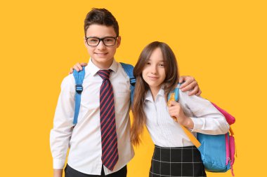 Sarı arka planda sırt çantaları olan sevimli okul çocukları.