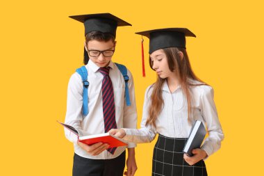 Mezuniyet şapkalı, sarı arka planda kitapları olan sevimli okul çocukları.