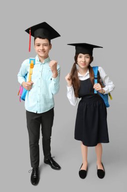 Mezuniyet şapkalı şirin okul çocukları gri arka planda kazanan jestler gösteriyor.