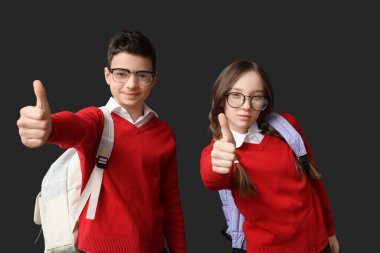 Koyu arkaplanda baş parmak hareketi gösteren sevimli okul çocukları.